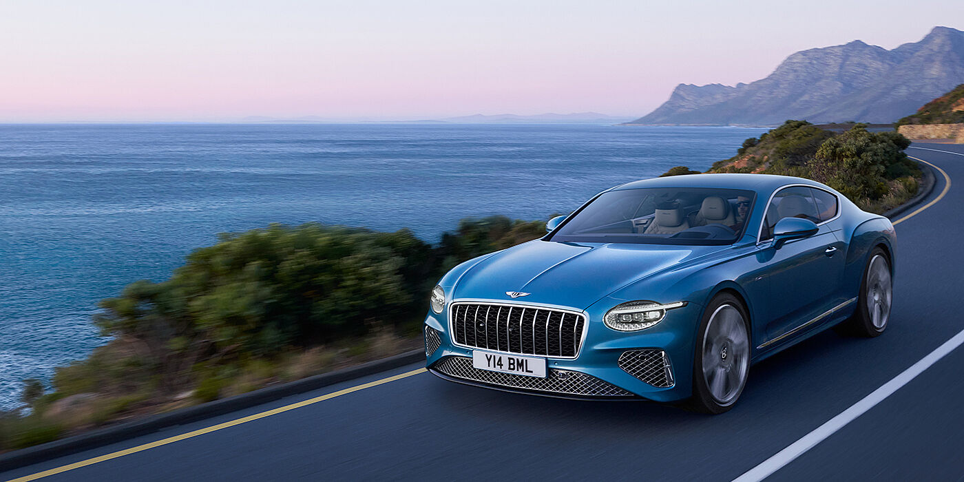 Bentley Singapore New Bentley Continental GT Azure coupe in Light Windsor blue paint with 22 inch Azure wheels and chrome grill, driving dynamically by the sea