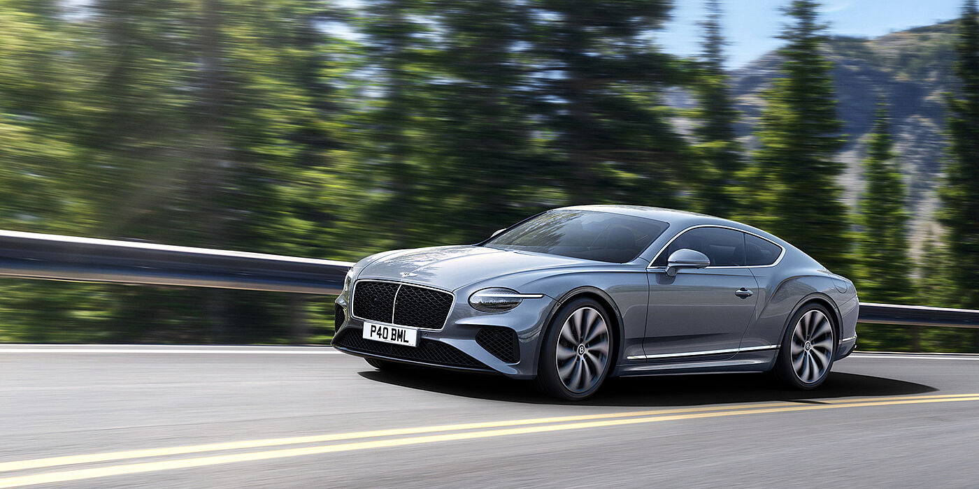 Bentley Singapore New Bentley Continental GT coupe in Silverlake paint and 22 inch ten-spoke wheels, driving dynamically on a tree-lined road in the sunshine