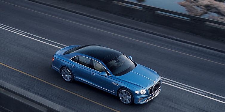 Bentley Singapore New Bentley Flying Spur Azure sedan in Light windsor blue paint by Mulliner, with 22 inch Azure wheels seen from overhead driving dynamically on a country road