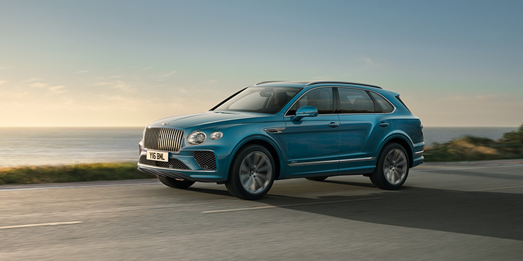 Bentley Singapore Bentley Bentayga Azure SUV in Topaz blue paint driving dynamically by the ocean with 22 inch 10 spoke directional wheels