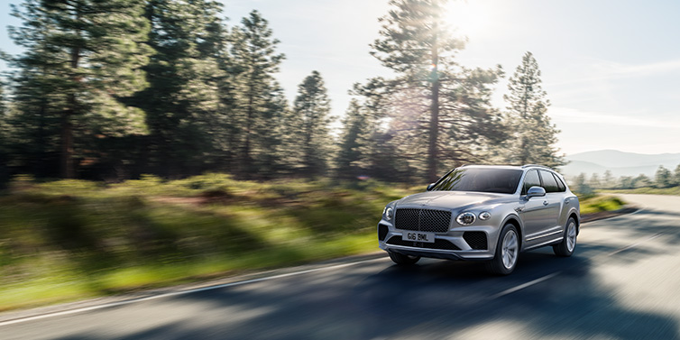 Bentley Singapore Bentley Bentayga SUV front three quarter in Moonbeam silver paint driving dynamically along a tree-lined road