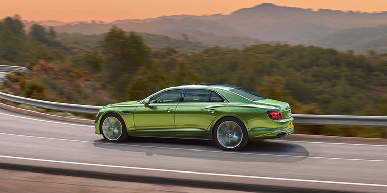 Bentley Singapore Bentley Flying Spur Speed sedan side profile in Tourmaline Green paint driving dynamically on a mountain road at sunset