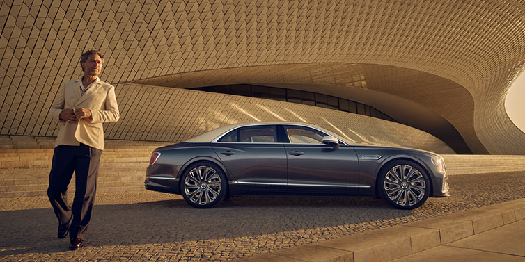 Bentley Singapore Bentley Flying Spur Mulliner sedan in Rose Gold over Magnetic duotone paint parked by a curved wall with person in suit jacket standing on the left